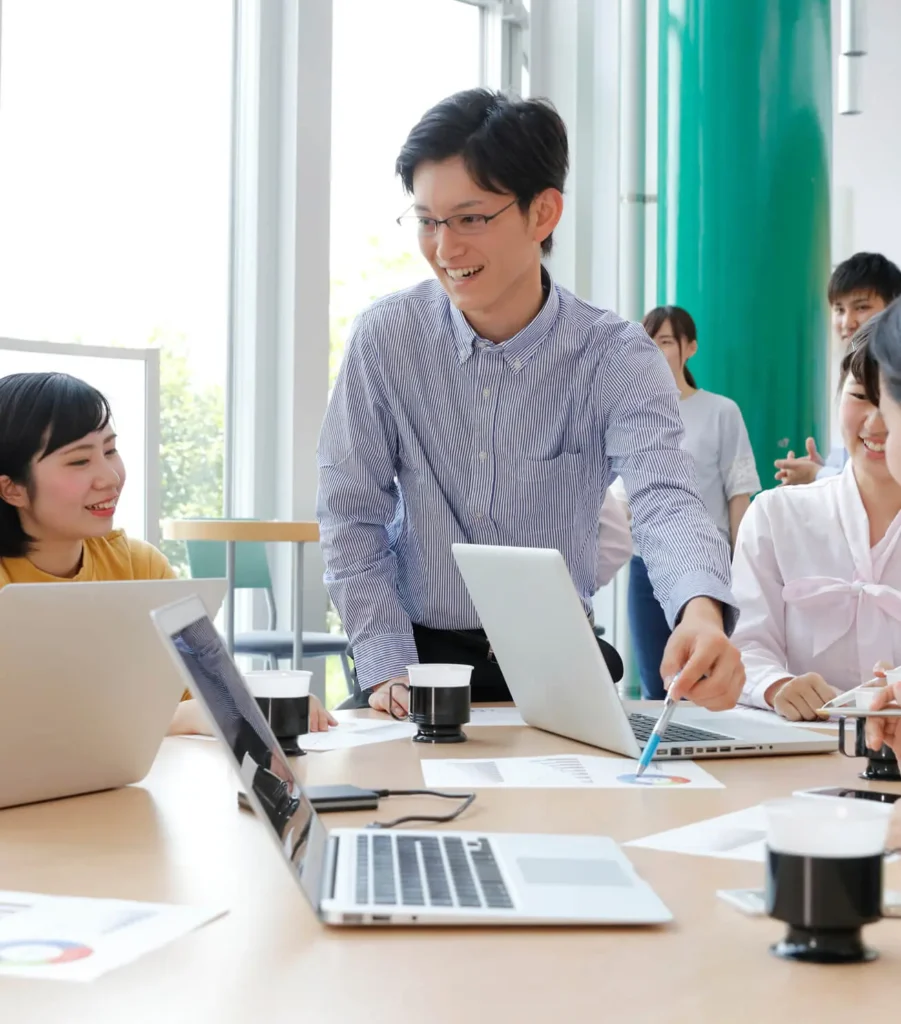 男性社員が他の社員にボールペンでグラフを指しながら説明している写真