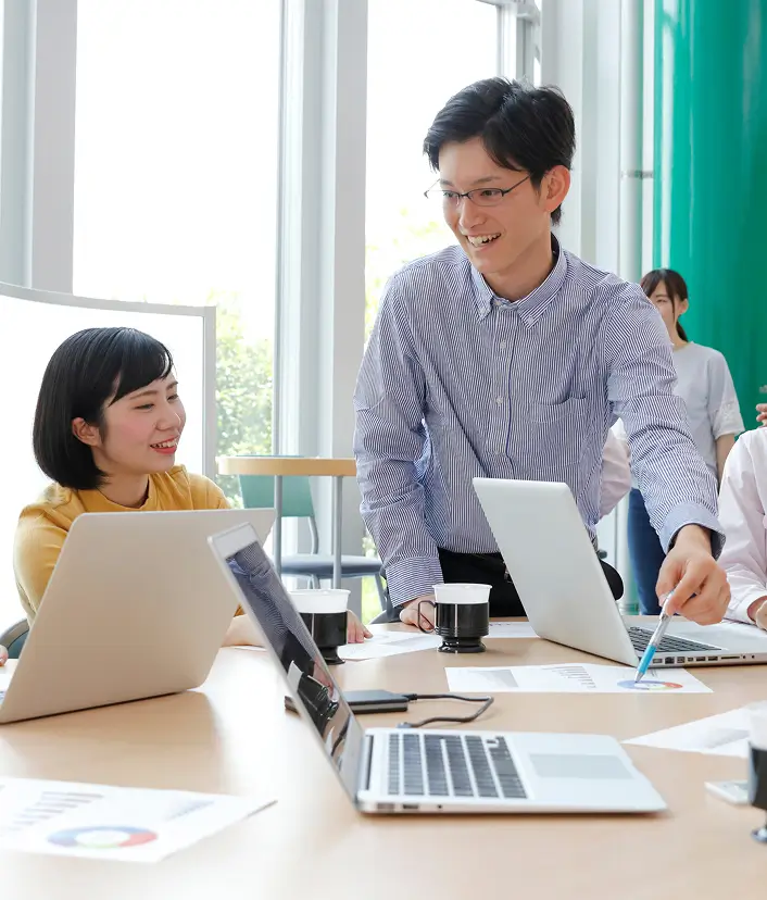 男性社員が他の社員にボールペンでグラフを指しながら説明している写真
